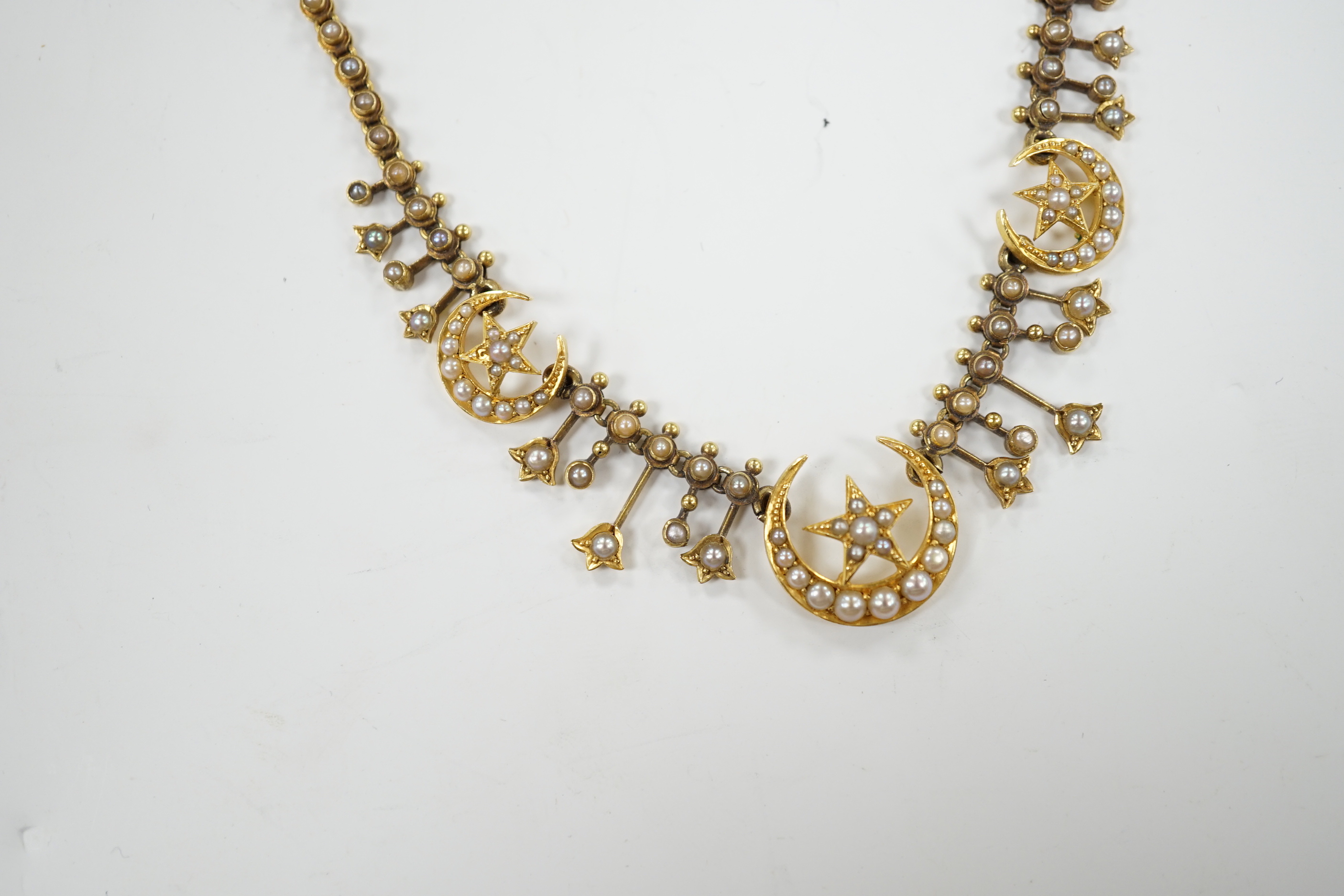 An Edwardian yellow metal and seed pearl set drop necklace, with star and crescent motifs, lacking central drop, 38cm, gross weight 16.3 grams.